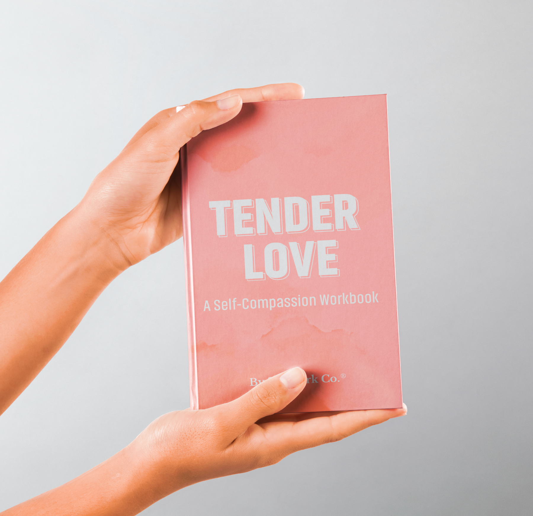 Hands holding SelfWork Co.'s Tender Love hardcover workbook with soft pink cover and bold embossed white title