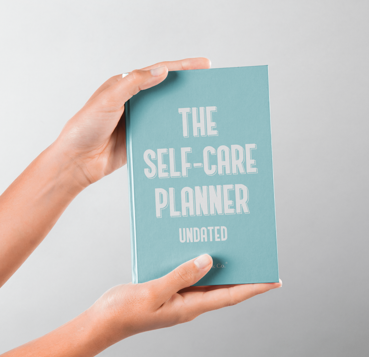 Person holding The Self-Care Planner hardcover book to display physical design and thickness